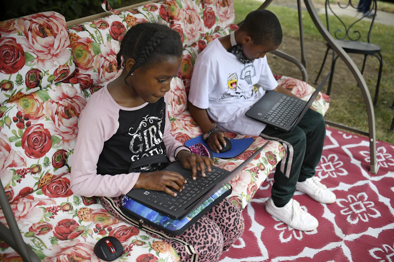 Fourth-grader Sammiayah Thompson, left, and her brother third-grader Nehemiah Thompson work outside in their yard on laptops provided by their school system for distant learning in Hartford, Connecticut.