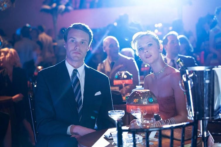 A young couple sit together in a theatre lounge setting.