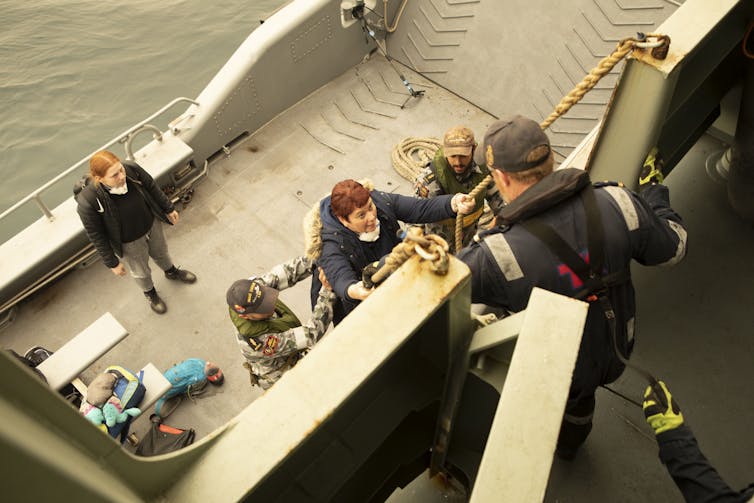 A female evacuee boarding a navy ship at sea.