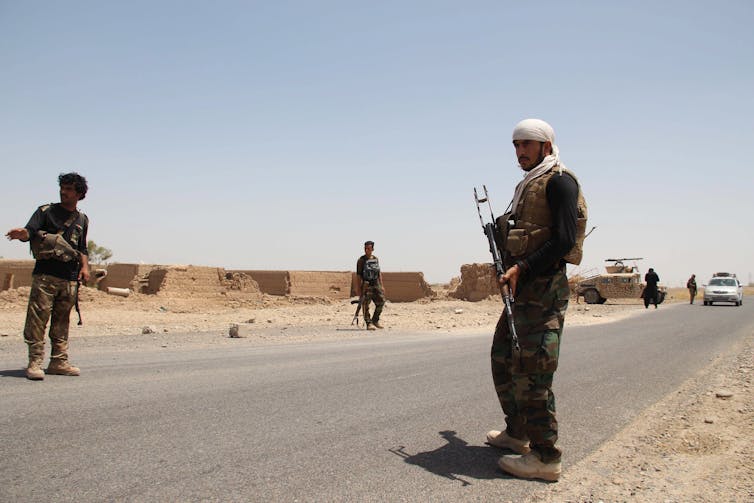 Afghan security officials standing guard on a road.