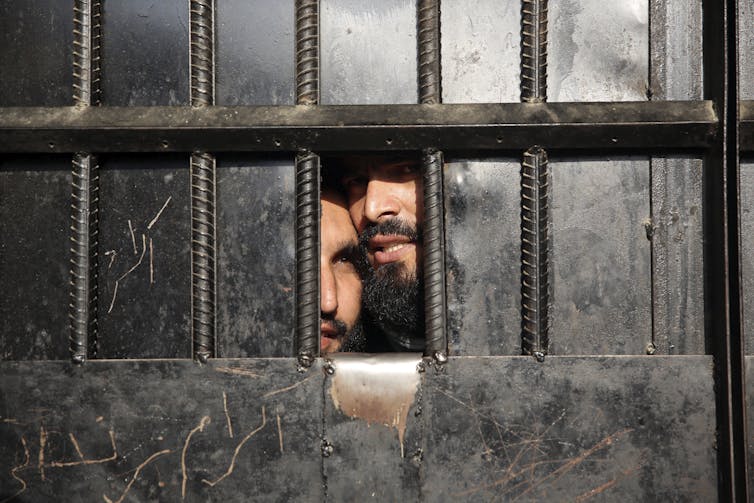 Taliban prisoners looking through a small window.