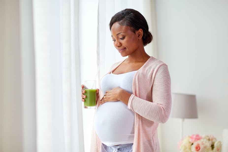 A woman places a hand on her pregnant belly while holding a glass of juice. 