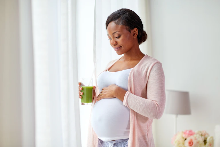 A woman places a hand on her pregnant belly while holding a glass of juice.