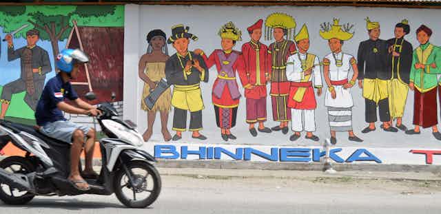 Pengendara melintas di depan sebuah mural bertemakan " Bhinneka Tunggal Ika" pada sebuah tembok.