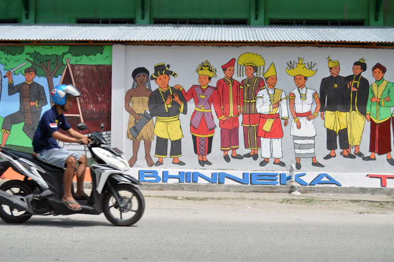 Pengendara melintas di depan sebuah mural bertemakan " Bhinneka Tunggal Ika" pada sebuah tembok.