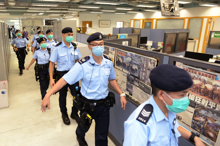 Line of police officers walks through newspaper office.