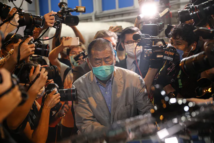 Jimmy Lai wearing face mask surrounded by photographers.