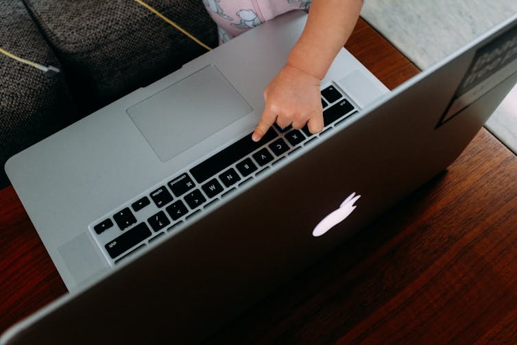 A toddler's hand reaches for a laptop keyboard.