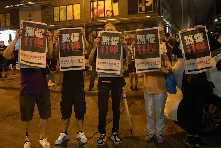 Street protestors hold signs in front of their faces.