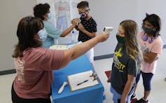 Two teachers standing with masks on checking students for fever with temperatures guns