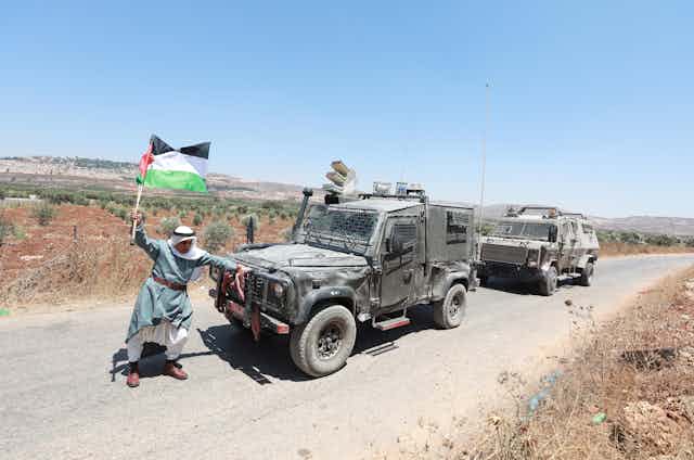 Elderly man with Palestinian flag confronts Israeli soldiers in armored vehicles
