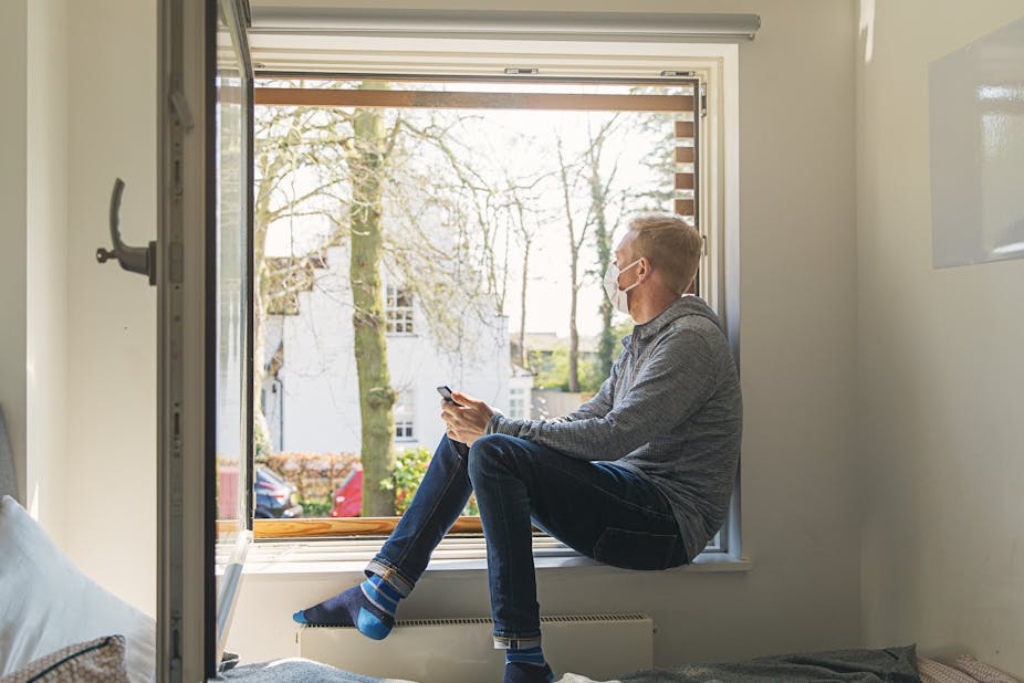 A man with a mask on sitting in a large open window.