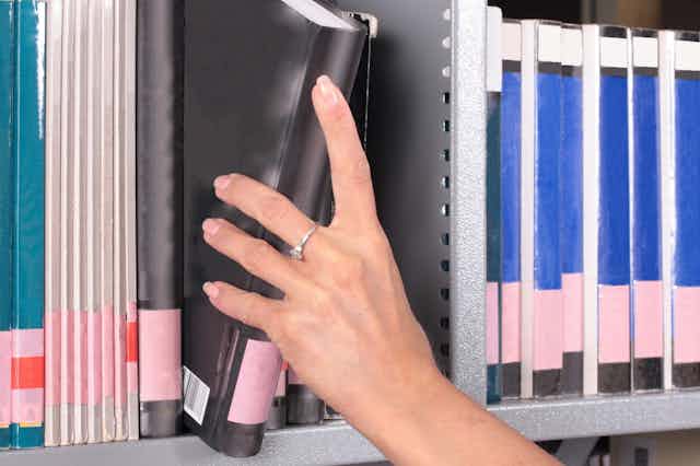 Hand removing a book from a shelf of journals and books