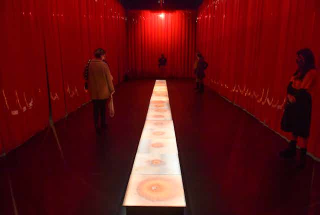 Red curtain around a floor projection with people exploring the space. 