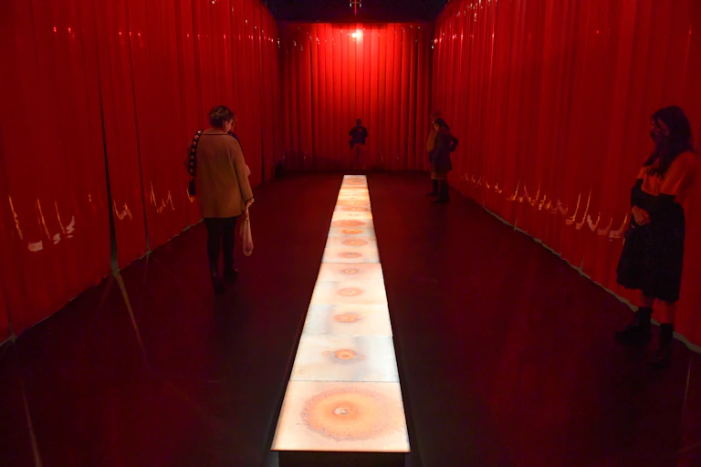 Red curtain around a floor projection with people exploring the space.