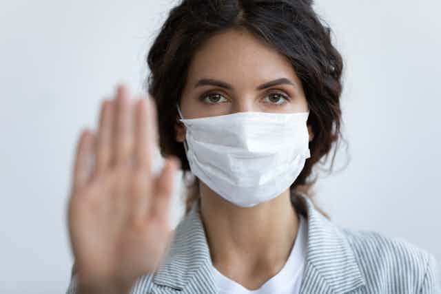 Woman wearing a mask and holding a blurred palm up to the camera, to say stop.