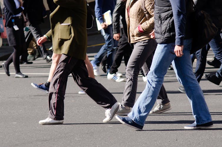 A crowd of people walking on the street. Their heads are cut off.