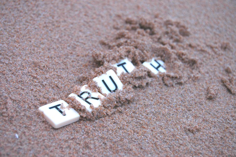 Letter tiles spelling 'truth' being covered up by sand.