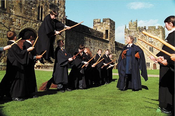 Junge Menschen in schwarzen Gewändern versuchen im Harry-Potter-Film Besen zu reiten.