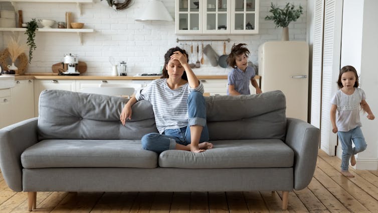 Mother looking exhausted on the sofa while children run around.