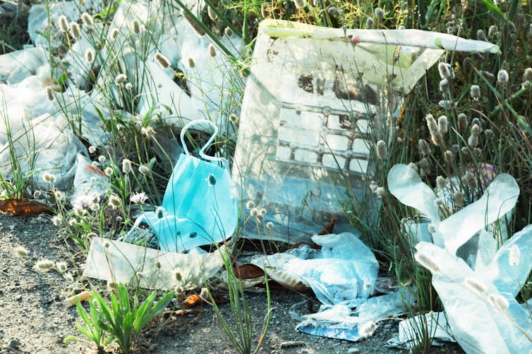 Discarded plastic waste in a grassy area, including plastic gloves and face masks.