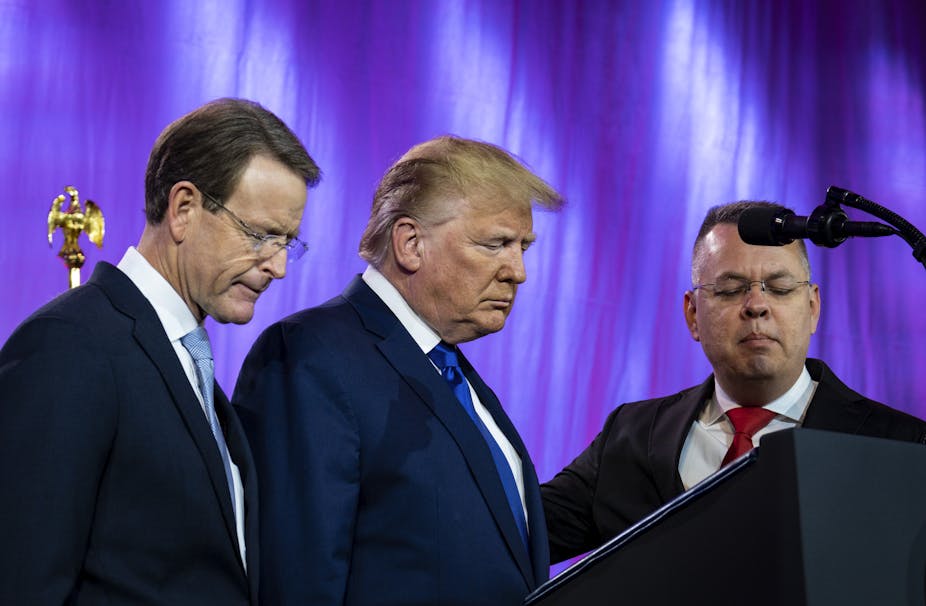 Three men including Donald Trump praying in front of a lectern. 