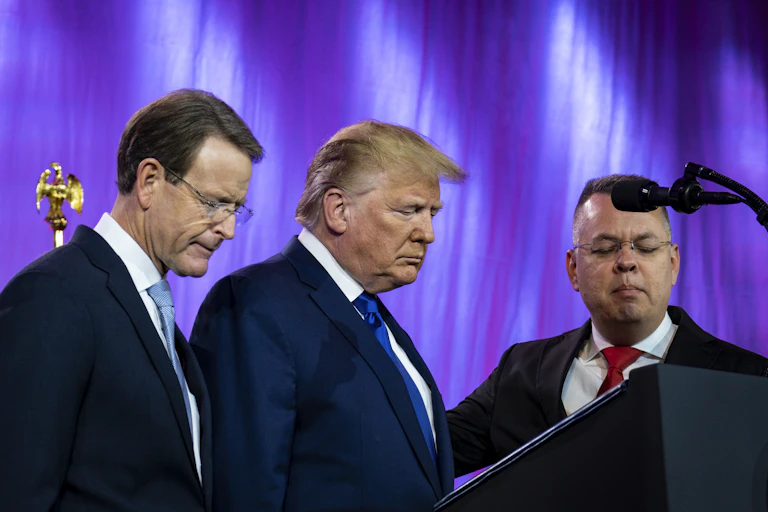 Three men including Donald Trump praying in front of a lectern.