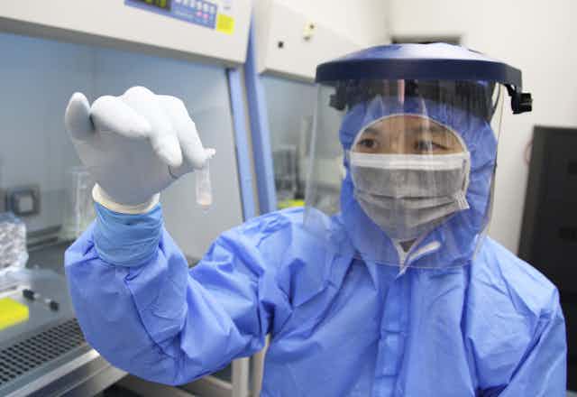 Scientist in personal protective gear holds tube of bone powder