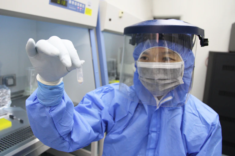 Scientist in personal protective gear holds tube of bone powder