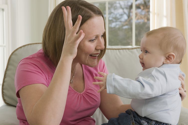 A white mother signing to her attentive baby who is mimicking the hand gesture