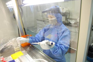 Ccientista em pipetas de equipamento de proteção sob um capuz