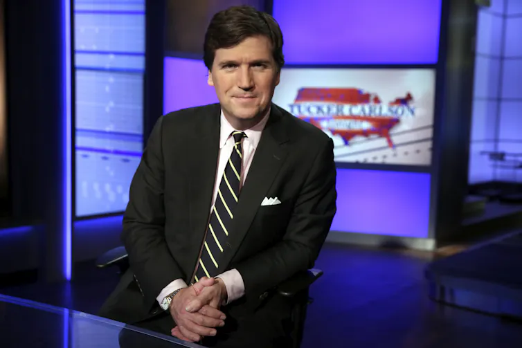 A portrait of Fox News host Tucker Carlson posing on the set of this TV show
