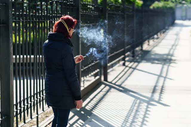 Una mujer fuma junto a la reja de un parque en Granada.