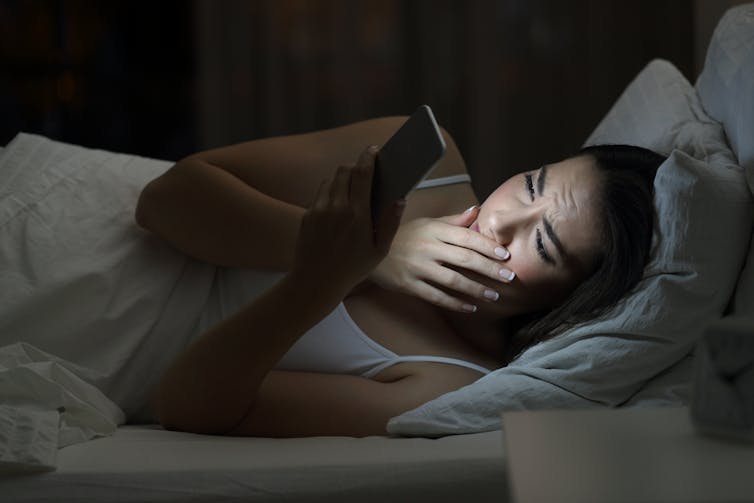 Young woman in bed at night using mobile phone.