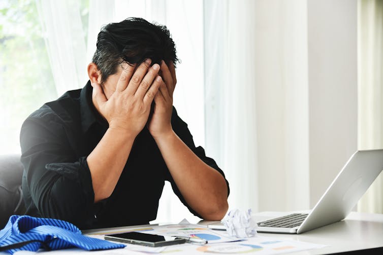 Man with head in hands at a laptop.