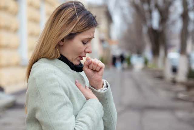 A woman is coughing outside in the street.