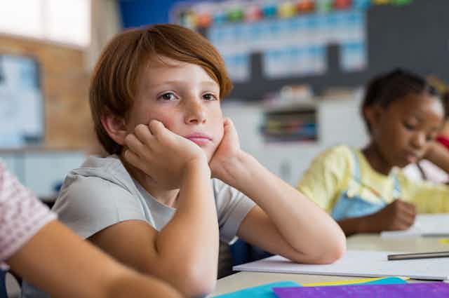 Boy looking sad or thoughtful sitting in class with chin in his hands.