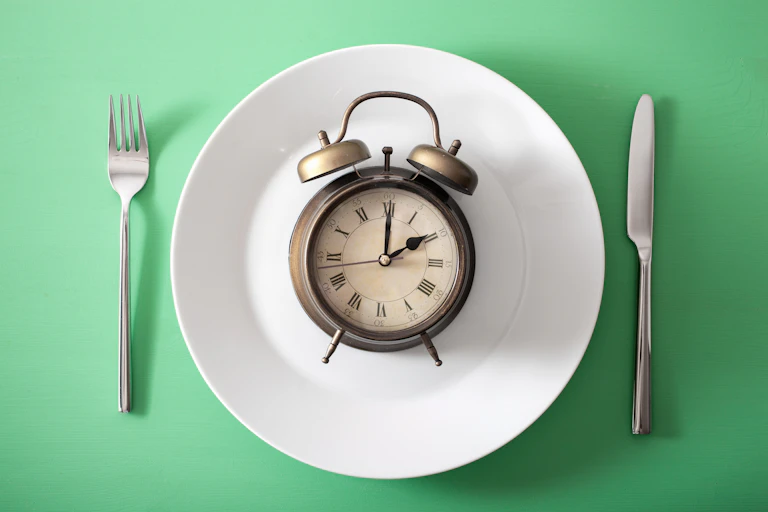 Clock on a white plate with a fork and knife on either side.