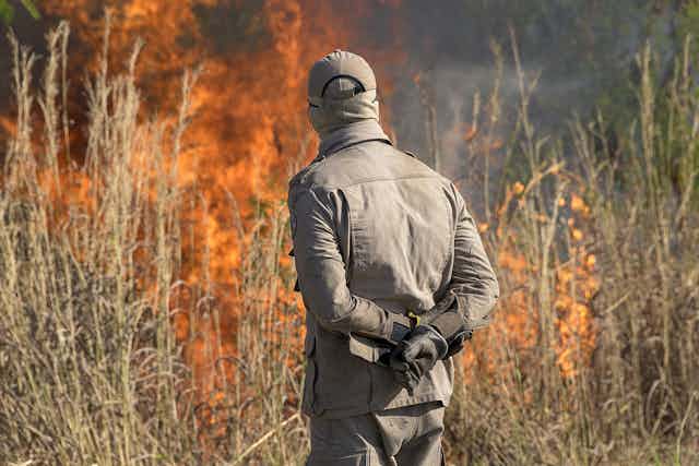 A firefighter stands inspecting a blaze in dry grass.