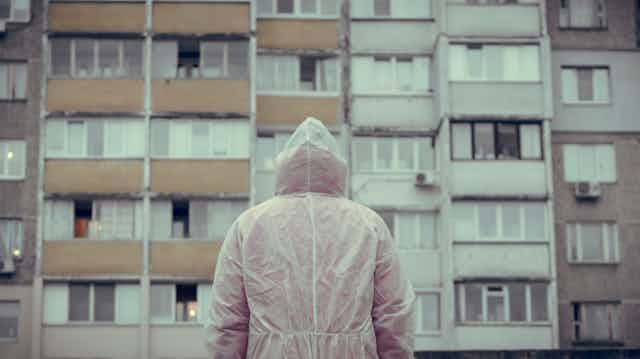 Una persona con un buzo blando, de espaldas, ante un edificio de viviendas.