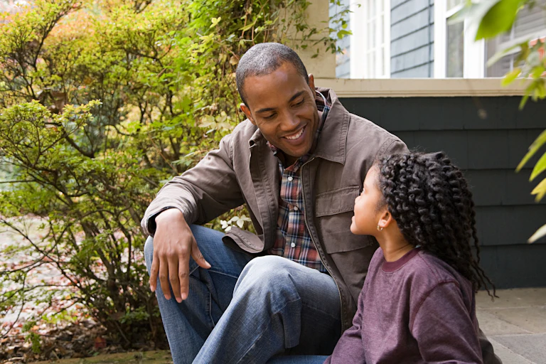 A father sits with a daughter talking outside.