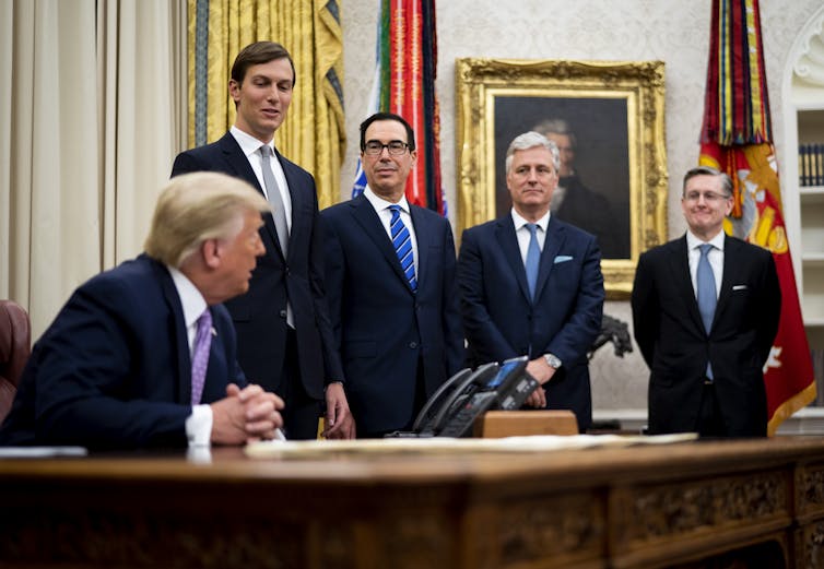 Trump sits next to his standing advisors in the Oval Office