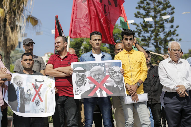 Palestinians hold signs with red X across the faces of US, Israeli and Emirati leaders
