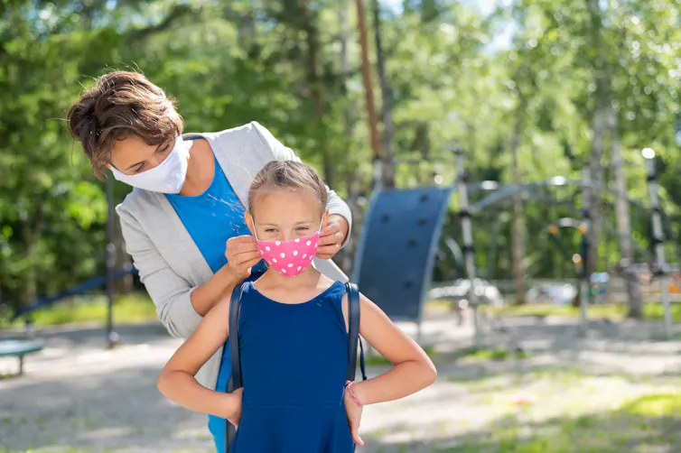 A mother helps her daughter adjust her face mask.