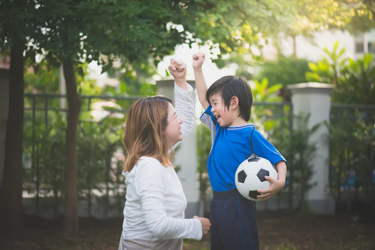 A mother crouches before her young son who holds a soccer ball.