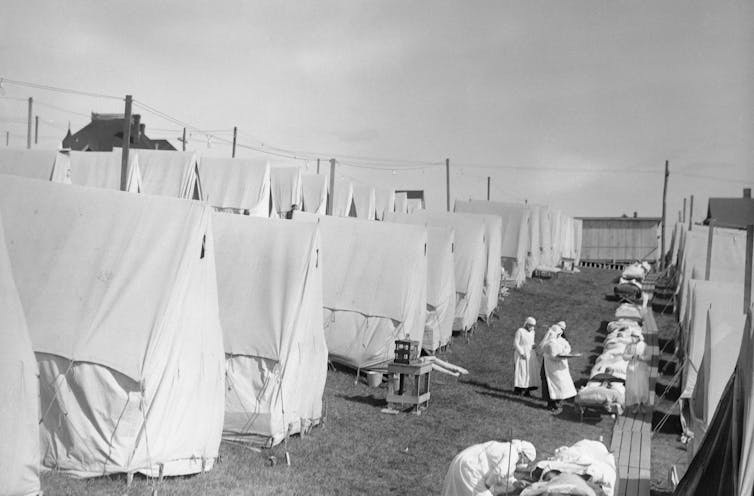 Patients lie on outdoor beds at flu camp filled with rows of tents.