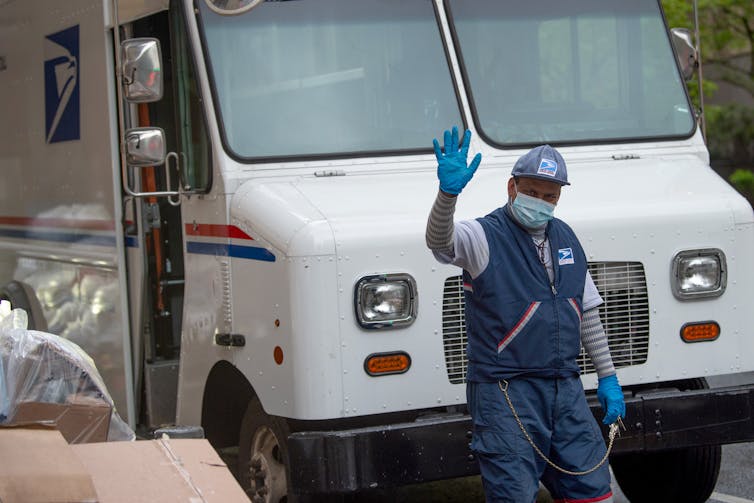 A mailman wearing a mask waves.