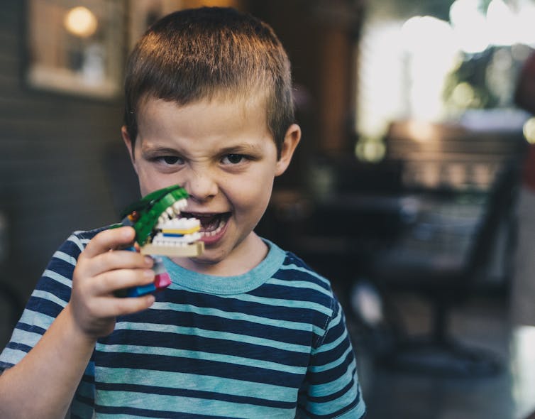 Little boy holding up set of toy teeth.