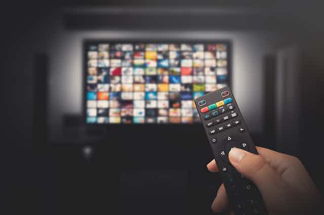 A tv with video thumbnails in the background and a hand holding a remote in the foreground