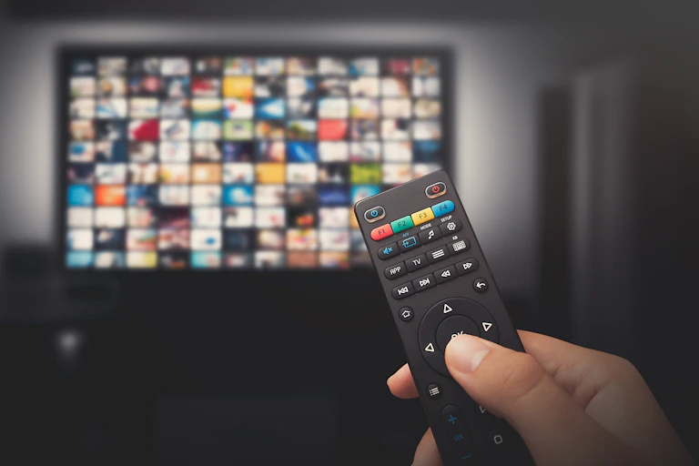 A tv with video thumbnails in the background and a hand holding a remote in the foreground